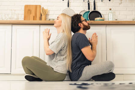 calm caucasian couple sitting on lotus pose on the floor at home and meditating during their self-care routine. High quality photoの写真素材
