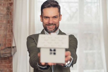 proud caucasian real estate agent advertisement presenting model house held in both palms. High quality photoの写真素材