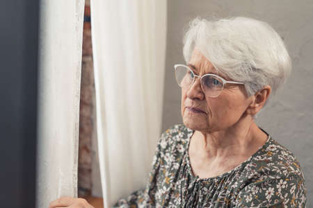 bothered upset grey-haired grandmother wearing glasses and peeking through the window. High quality photoの写真素材