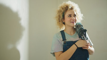 Smiling curly hair girl holding big drill hammer and thinking about decorating new house. High quality photoの写真素材