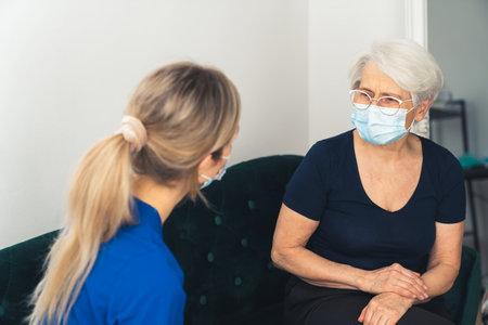 Home visit concept. Masked senior explaining her health problems to her primary care physician lady. . High quality photoの写真素材
