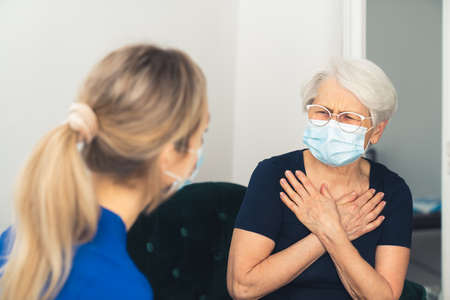 Elderly lady feeling bad and sick, touching her chest, and complaining about heart pain to her caregiver. High quality photoの写真素材