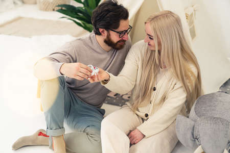 Young Caucasian couple sitting on the floor in the childrens room looking at each other holding childrens shoe. High quality photoの写真素材