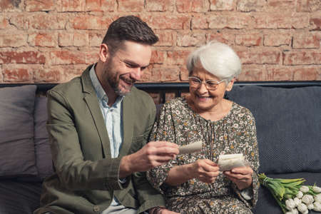 portrait of two relatives bonding and laughing while looking at old vintage photographs that belong to elderly woman. High quality photoの写真素材