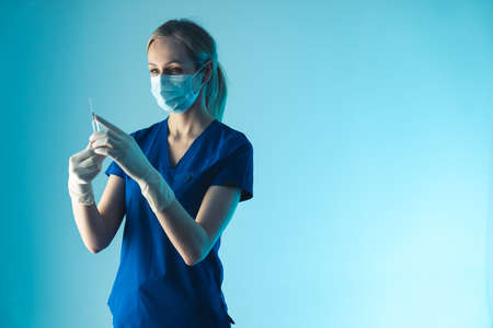 Masked caucasian doctor wearing a uniform with an injection in her hands. Healthcare and prevention of disease. High quality photoの写真素材