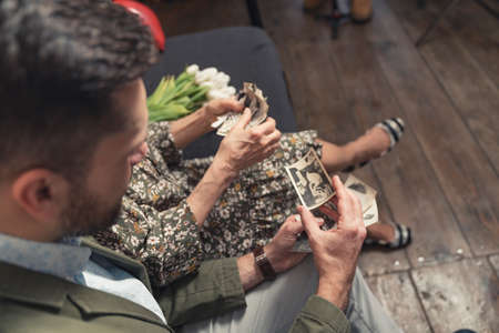 two caucasian relatives touching and watching small old black-and-white vintage photographs on...