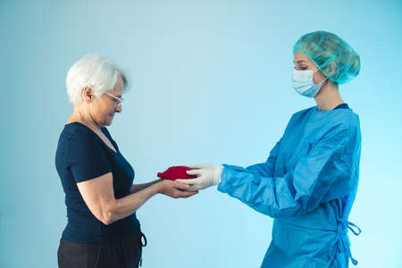 Young caucasian female surgeon passing artificial heart model to elderly european grey-haired woman. The importance of taking care of ones health. High quality photoの写真素材