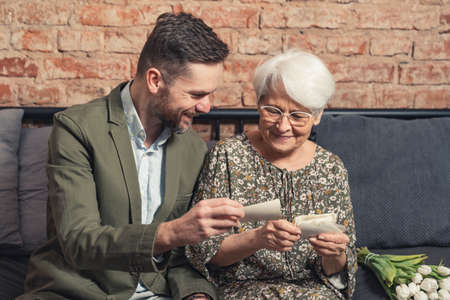 elegant elderly pensioner lady bonding with her adult grandchild by looking at old photos and talking about her life. High quality photoの写真素材