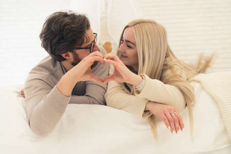 adorable young couple lying on the bed making a heart shape together with their hands. High quality photoの写真素材