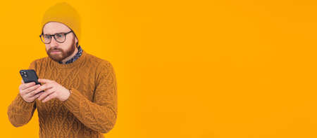 Confused bearded Caucasian man using his smartphone looking at it portrait orange background...
