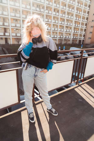 Vertical shot of young blond woman enjoying beautiful weather by walking down her neighborhood, listening to music on her old-fashioned portable cassette player. High quality photoの写真素材