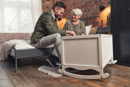 middle-aged man and his grey-haired retired mother talking and laughing over the white crib. High quality photoの写真素材