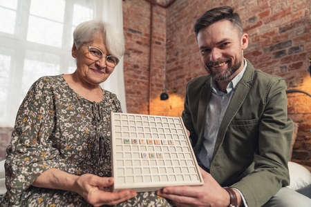 caucasian elderly pensioner mother and her middle-aged elegant son presenting to camera a crossword with a caption Mothers Day . High quality photoの写真素材