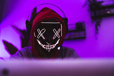 Masked hacker in action. Safety in the internet concept. Magenta color. High quality photoの写真素材