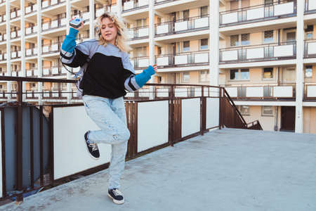 90s adolescence concept. Full outdoor shot of dancing blonde-haired woman in her 20s in baggy jeans holding her old-fashioned vintage music player. High quality photoの写真素材