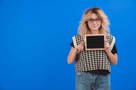 Beautiful caucasian woman wearing glasses and holding tablet or blackboard to camera. Copy space. Isolated. Blue background. . High quality photoの写真素材