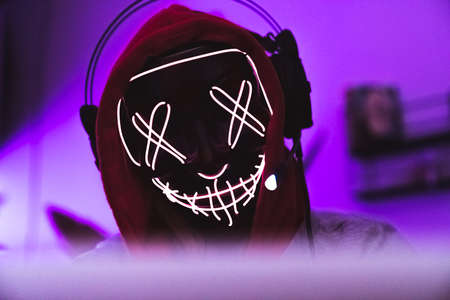 Masked hacker concept. Identity and data protection. Headphones and red hood. Magenta background. High quality photoの写真素材