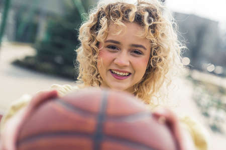 Beautiful young blond woman smiles and holds a basketball ball in front of her closeup copy space . High quality photoの写真素材