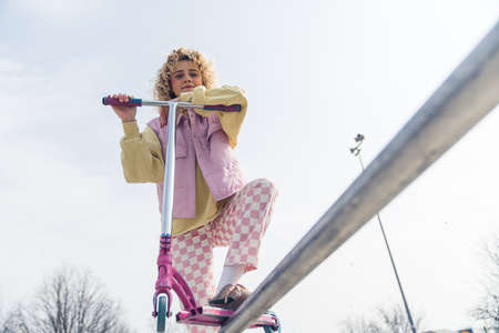 Beautiful young blond woman posing with a pink scooter, smiling and looking at the camera active lifestyle concept copy space medium full shot. High quality photoの写真素材