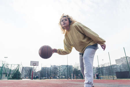 Young blond Caucasian woman plays basketball in baggy clothes, looking up copy space medium full shot . High quality photoの写真素材