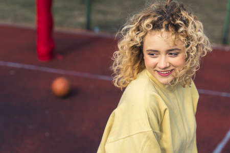 Portrait of young blond Caucasian woman on the sports field in the light yellow sweater, looking away copy space . High quality photoの写真素材