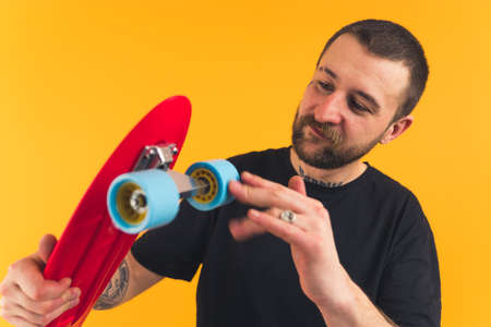 young satisfied personable bearded European man holding a skateboard orange background studio shot...