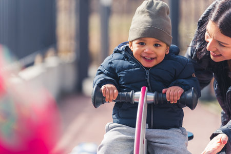 Happy joyful multiracial child has fun in the playground. Little boy supported by his dedicated...