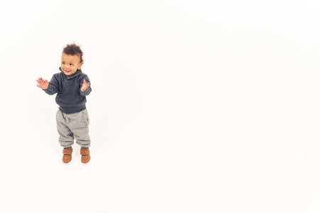 Curiosity concept. Young biracial toddler in warm clothes standing and clapping his hands over white...