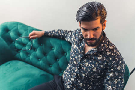 young good-looking hispanic man siiting on sofa looking thoughtful indoor studio shot medium shot . High quality photoの写真素材