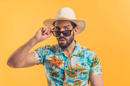 Shot of handsome bearded Latin man wearing modern sunglasses and hat - smiling over orange studio background - isolated. High quality photoの写真素材