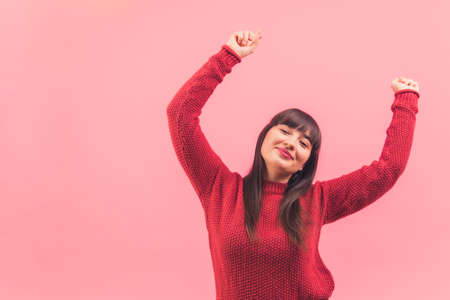Attractive young dark haired woman dancing, holding her hands up isolated pink background copy space portrait . High quality photoの写真素材