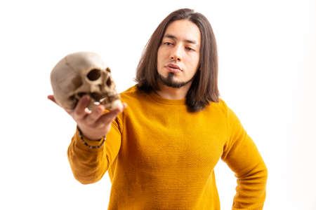Young Caucasian bearded man holds skull and looks at it white background studio shot isolated . High quality photoの写真素材