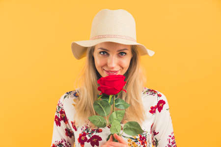 elegant blonde European girl holding a red rose and smiling medium closeup yellow background studio shot beauty concept. High quality photoの写真素材