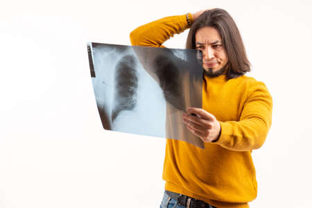 Young man looking at lung x-ray, frowning and touching head with his hand isolated studio shot copy...