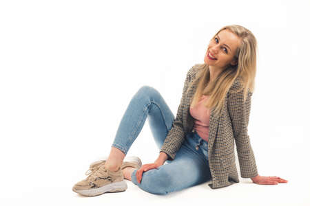 Cheerful smiling beautiful caucasian young woman looking at camera while sitting in a studio over white background. Sport casual fashion. High quality photoの写真素材