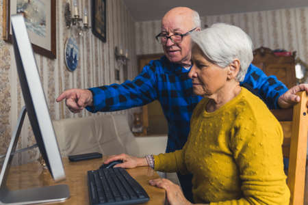 Modern seniors concept. Caucasian grandmother learns how to use a computer with the help of her pensioner bald husband. High quality photoの写真素材