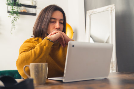 Young European dark-haired man looking at the screen of laptop, working at home in casual clothing home-based job concept . High quality photoの写真素材