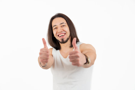 Young handsome smiling man showing thumbs up to the camera isolated studio shot copy space white background . High quality photoの写真素材