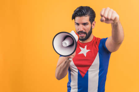 Latino American man with the Cuban flag on T-shirt shouting in megaphone medium shot studio shot orange background . High quality photoの写真素材