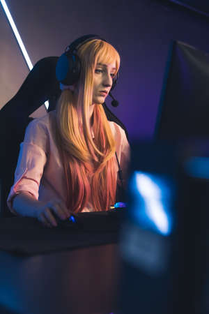 young Caucasian professional gamer girl playing and streaming online game medium closeup indoors cyber sport concept neon light. High quality photoの写真素材