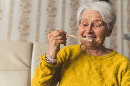 European elderly short-haired senior lady holding ecological bamboo toothbrush and brushing her teeth. The importance of hygiene. . High quality photoの写真素材