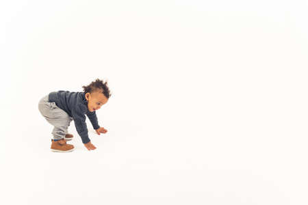 Curious biracial toddler boy trying to stand up in studio over white background. Child development...