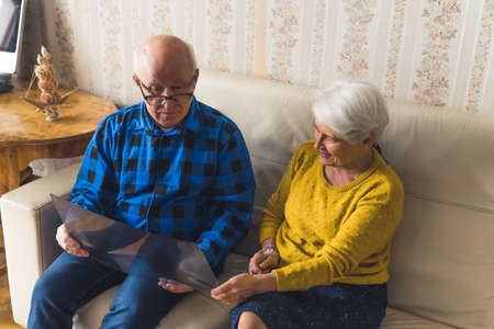 Pensioner caucasian spouses looking at x-ray results while sitting on a beige leather sofa. Support during illness. High quality photoの写真素材