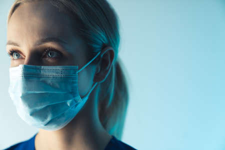portrait of a beautiful blonde young Caucasian nurse with a surgical mask closeup blue background studio shot medical concept. High quality photoの写真素材