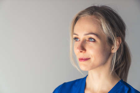 young charming blonde European nurse looking satisfied closeup studio shot grey background copy...