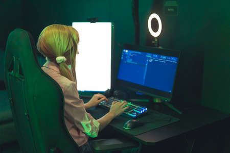 Young caucasian blonde gamer girl using colorful illuminated keyboard using her professional desktop...