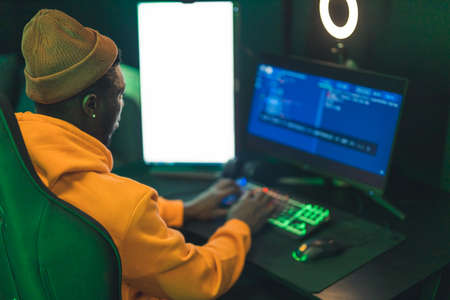 African-American casually dressed male freelance programmer sitting in a studio, clicking on keyboard, looking at computer screen. High quality photoの写真素材