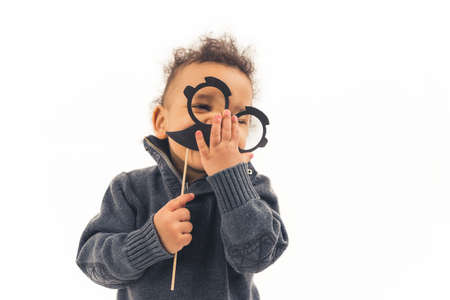 Funny happy biracial boy in a gray sweater holding black hipster mustache and glasses photo props...