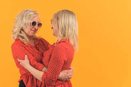 childhood and parenthood concept, mom and daughter embracing and hugging over orange background, isolated copyspace. High quality photoの写真素材