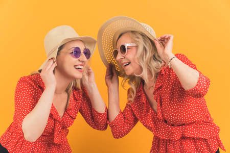 two attractive women together having fun, mother and daughter in similar clothes and hats smiling...
